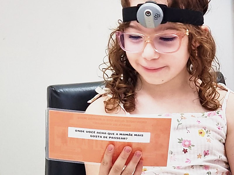 Menina com uma câmera pequena presa à cabeça lê uma carta do jogo usado na pesquisa.