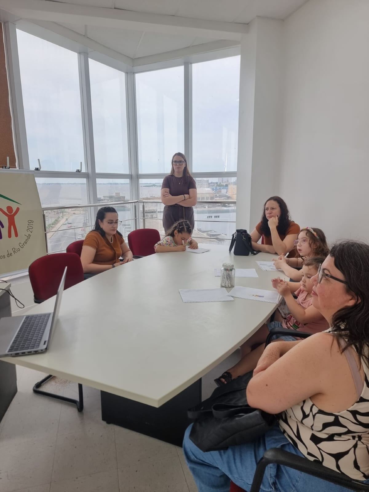 Mães e crianças da Coorte em volta de uma mesa durante uma oficina do GPIS, com crianças desenhando e escrevendo.